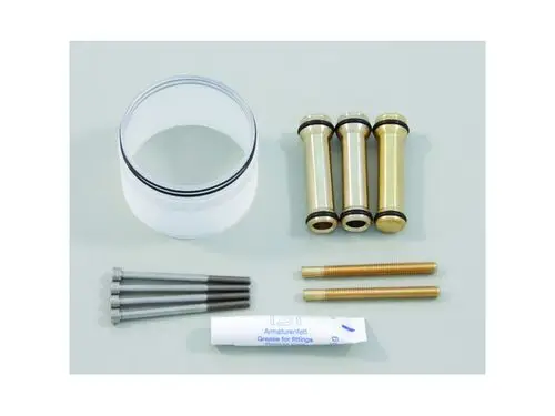 Ideal Standard Bauteile: Ein transparenter Zylinder mit O-Ringen, drei metallische Teile, zwei Schrauben und ein Tubus mit Schmiermittel auf einem flachen Untergrund.